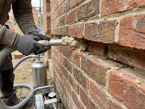 Doorsnede van een spouwmuur met isolatiemateriaal dat wordt ingespoten door een boorwerker met professionele apparatuur