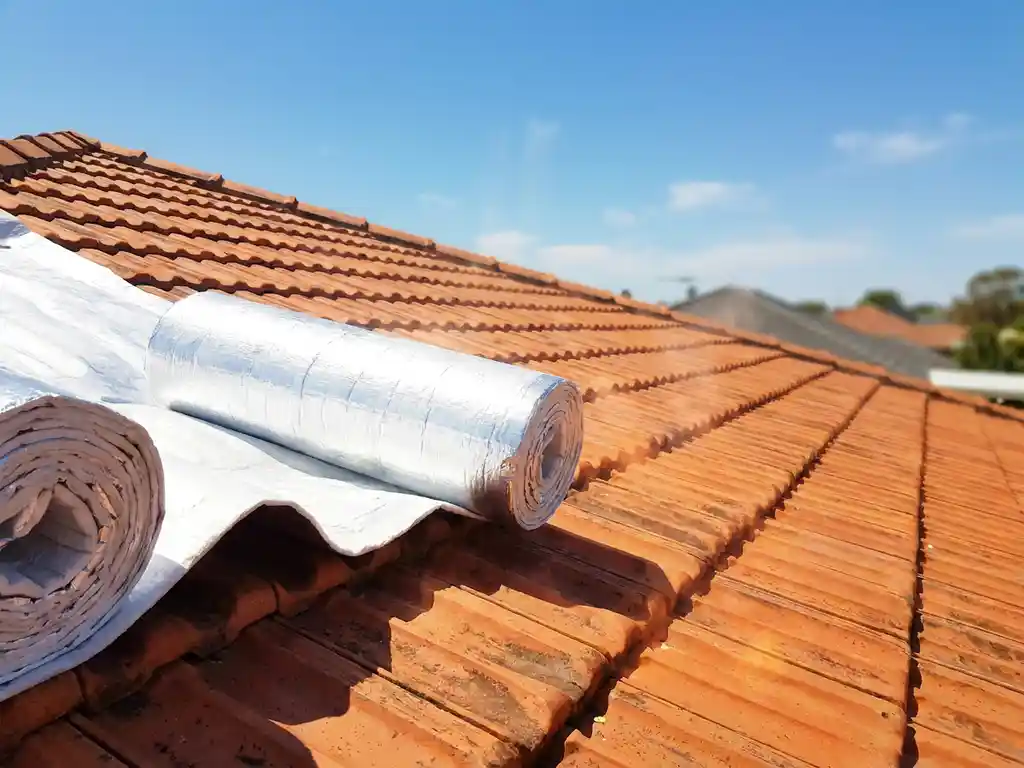 Terracottadak met uitgerolde reflecterende isolatie onder een heldere zomerse lucht, met warmtedistorsie boven de dakpannen.